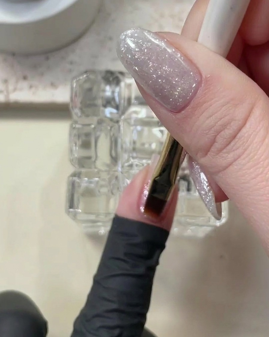 Ein Pinsel trägt eine dünne, klare Schicht Builder Gel auf einen mit Glitzer überzogenen Nagel auf.