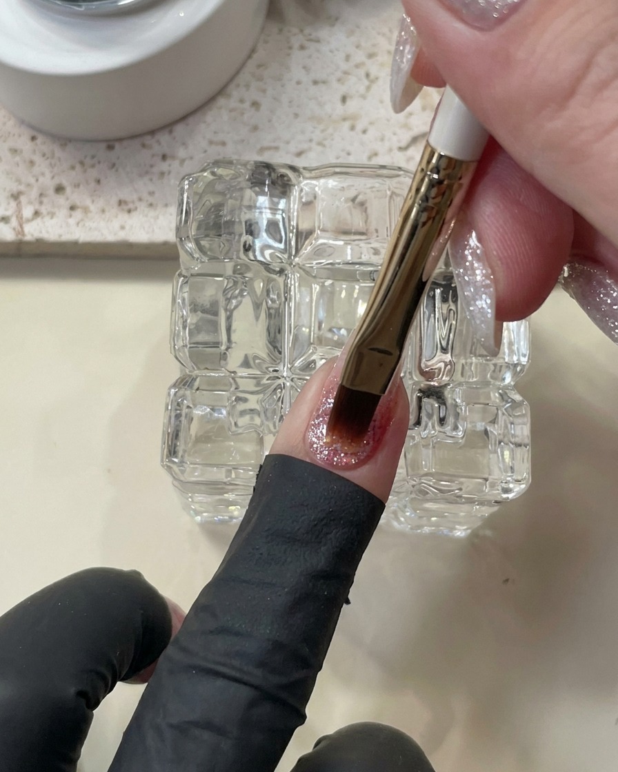 Ein Pinsel trägt einen dickeren, selbstglättenden Tropfen Builder Gel auf den Nagel auf.