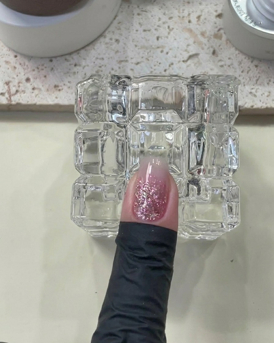Ein Finger mit aufgetragenem Builder Gel liegt unter einer UV/LED-Lampe.