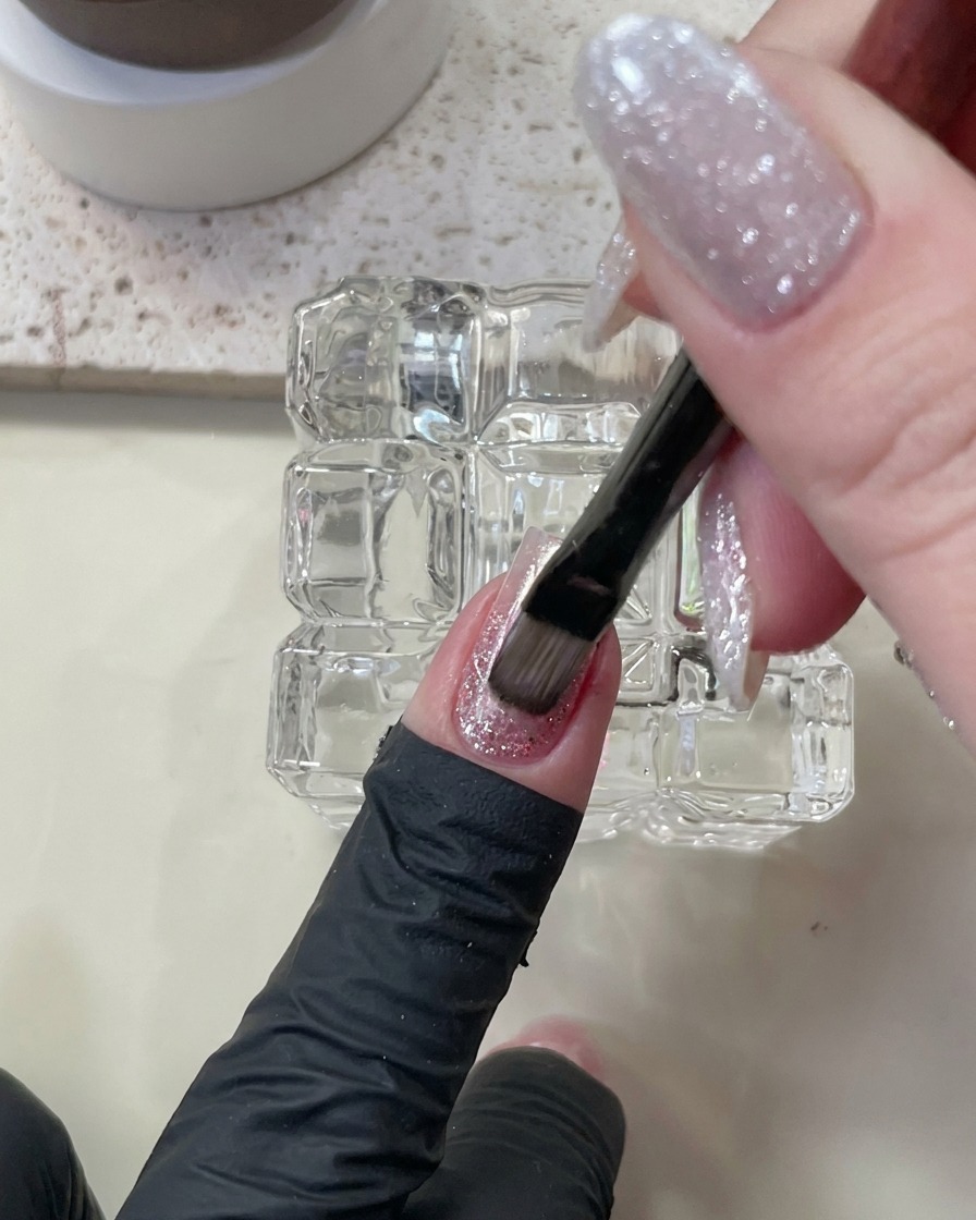 Ein Pinsel trägt Nude Cat-Eye-Gellack über die bestehenden Nagelschichten auf.