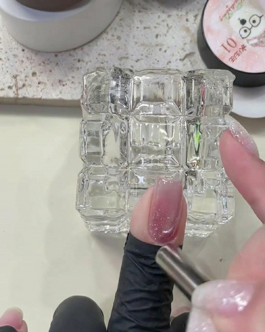 Nahaufnahme eines Nagels, der mit einem Magnetwerkzeug gehalten wird, um das magnetische Pigment über der Diamant-Glitzerbasis zu formen.