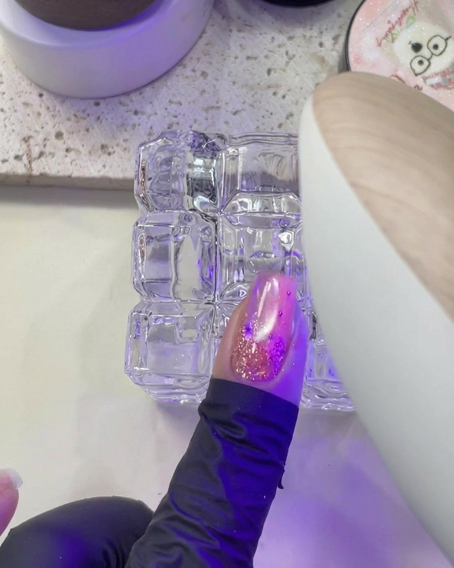 Eine Hand platziert einen Fingernagel unter dem violetten Licht einer UV/LED-Nagellampe zum Aushärten.