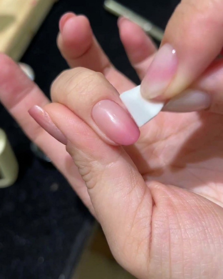 Eine Hand tupft mit einem Schwamm eine zweite Schicht rosa Cat-Eye-Gel auf einen Nagel.