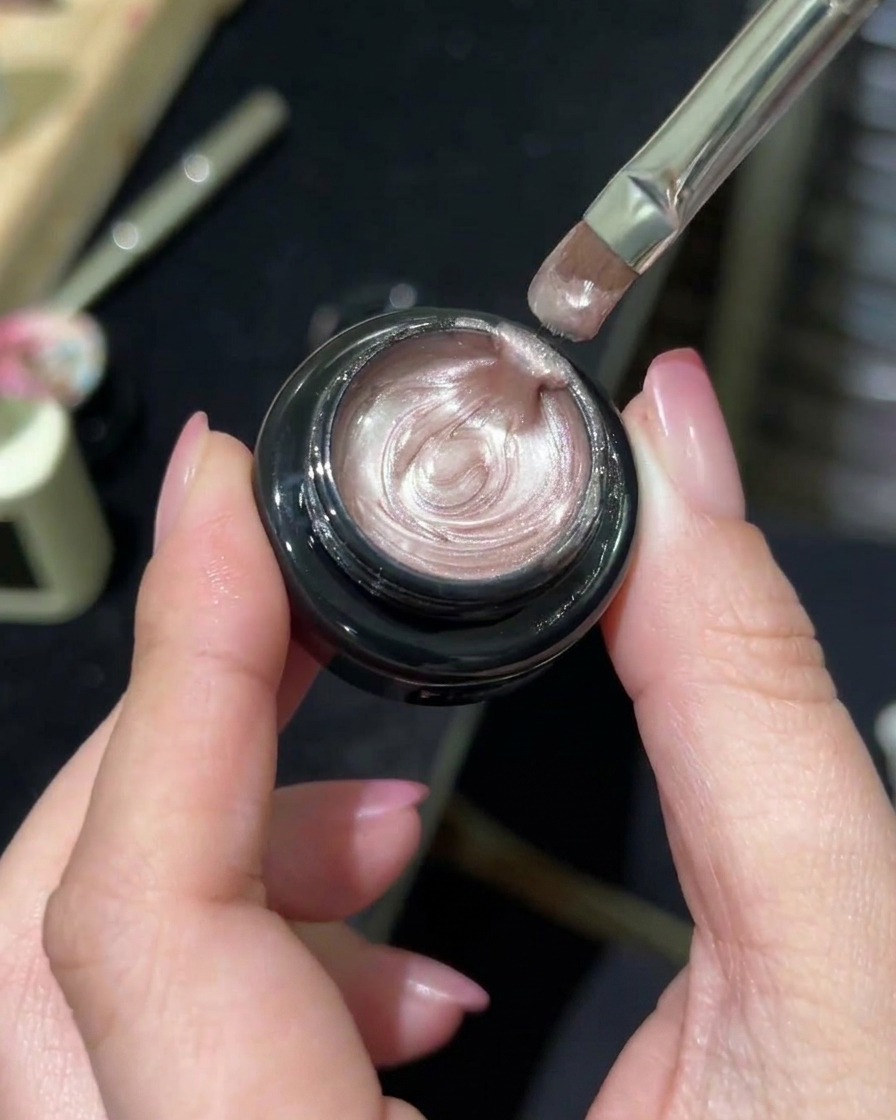Ein professioneller Nagelpinsel nimmt schimmerndes Aurora-Magnetgel aus einem Tiegel auf.