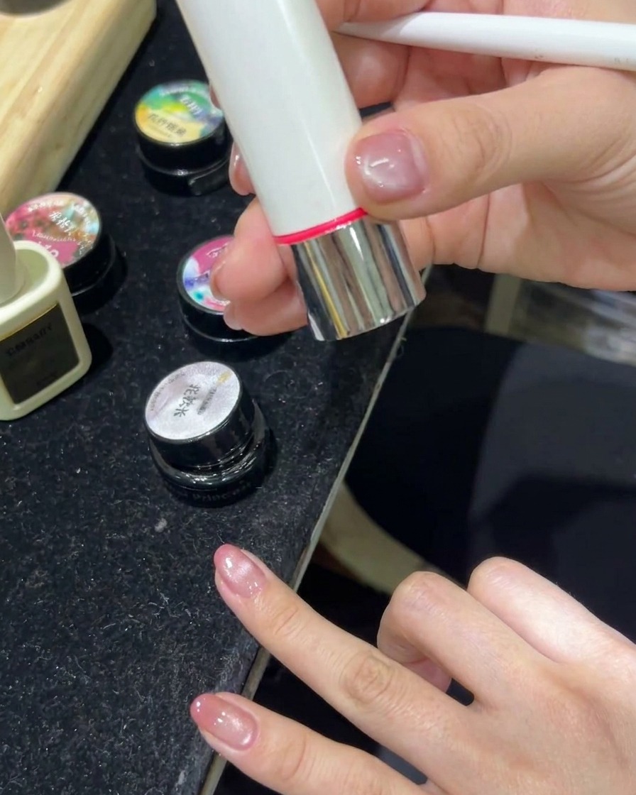 Eine Hand ruht in einer LED-Nagellampe, während das Licht eingeschaltet ist und die Cat-Eye-Gelnägel aushärtet.