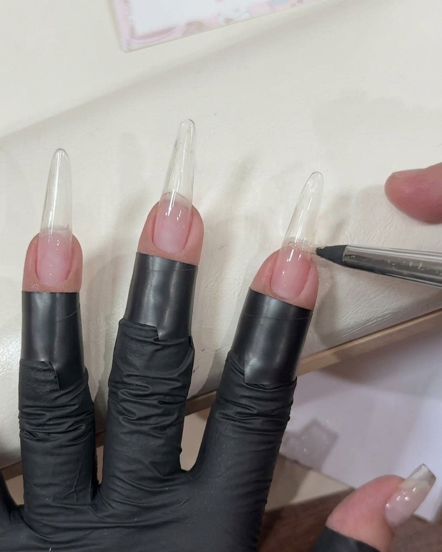 Auftragen eines transparenten hellrosa Gels auf eine lange, klare Nagelverlängerung mit einem flachen Pinsel.