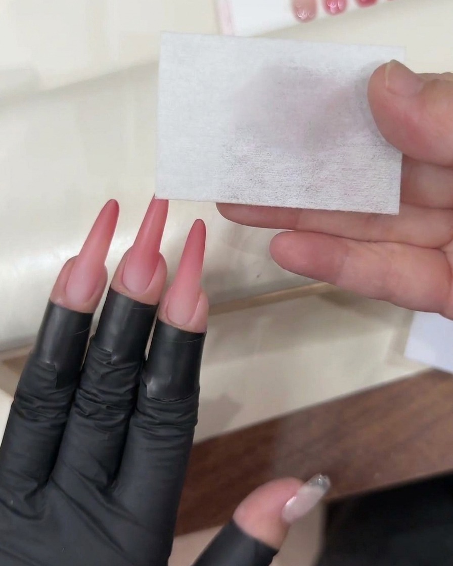 Ein Gel-Pinsel trägt einen klaren, glänzenden Top Coat auf den fertigen pinken Ombré-Nagel auf.