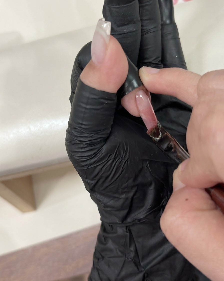 Eine Pinzette platziert vorsichtig ein kleines dekoratives Schmuckstück auf einen feuchten, mit Top Coat überzogenen Nagel.