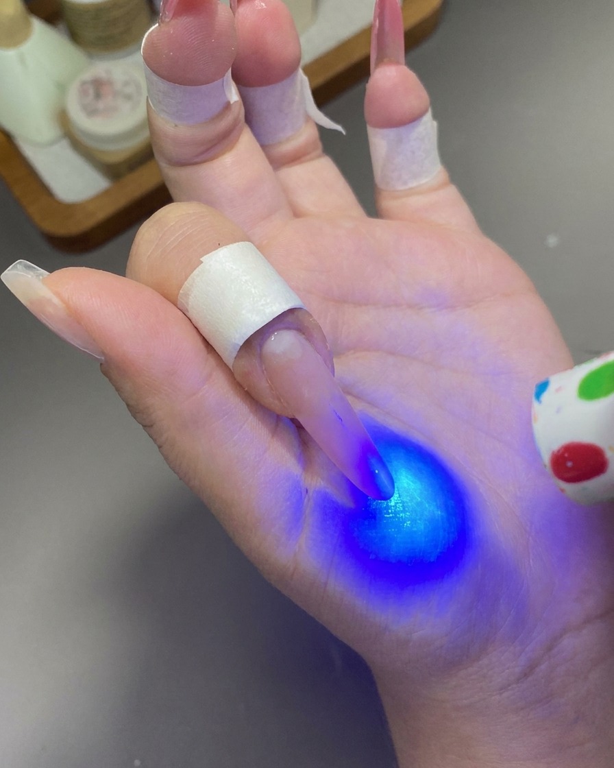 Eine kleine Hand-UV/LED-Lampe härtet das Gel auf einem Fingernagel mit blauem Licht aus.