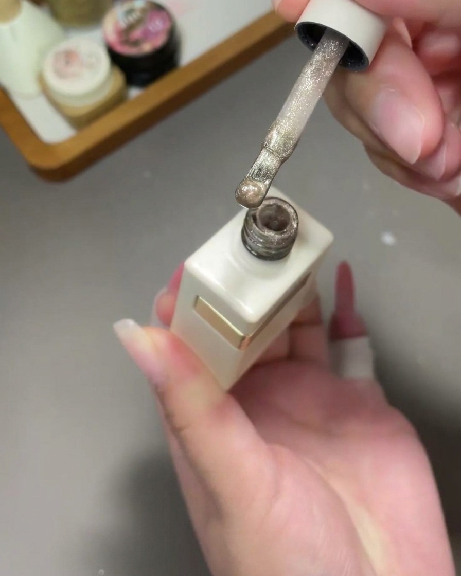 Ein Pinsel trägt schimmerndes goldenes Cat-Eye-Gel über einen rosa Verlaufsnagel auf.