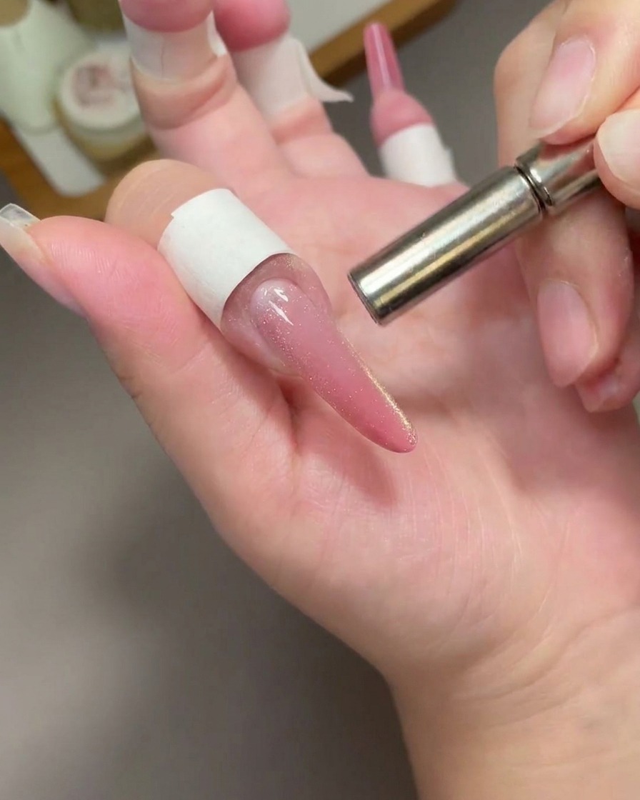 Ein zylindrischer Metallmagnet schwebt über einem langen rosa Cat-Eye-Nagel, um die Partikel zu bewegen.
