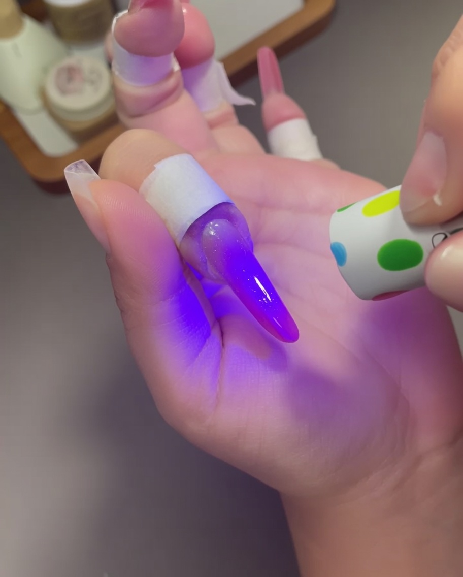 Eine gepunktete Mini-UV-Lampe wird über einen Finger mit einem violett-rosa Cat-Eye-Design gehalten.