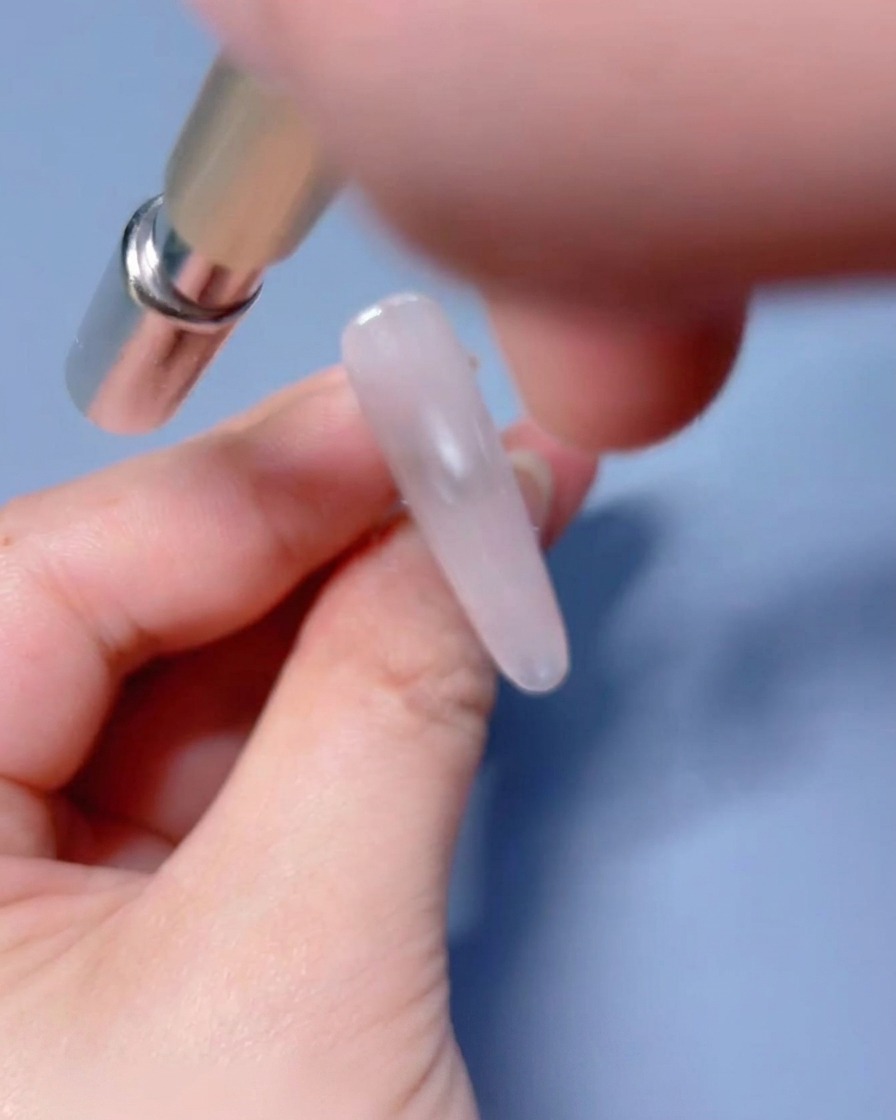 Ein Magnetwerkzeug wird nahe an den feuchten, mit Gel beschichteten Nagel gehalten, um die Schimmerpartikel zu bewegen.