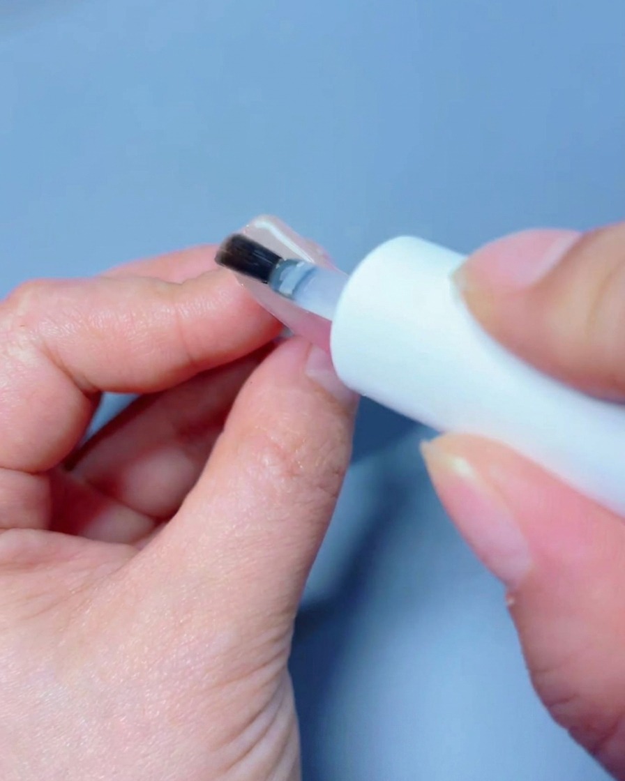 Eine Hand wird unter einer professionellen UV/LED-Nagellampe platziert, um den Top-Coat auszuhärten.