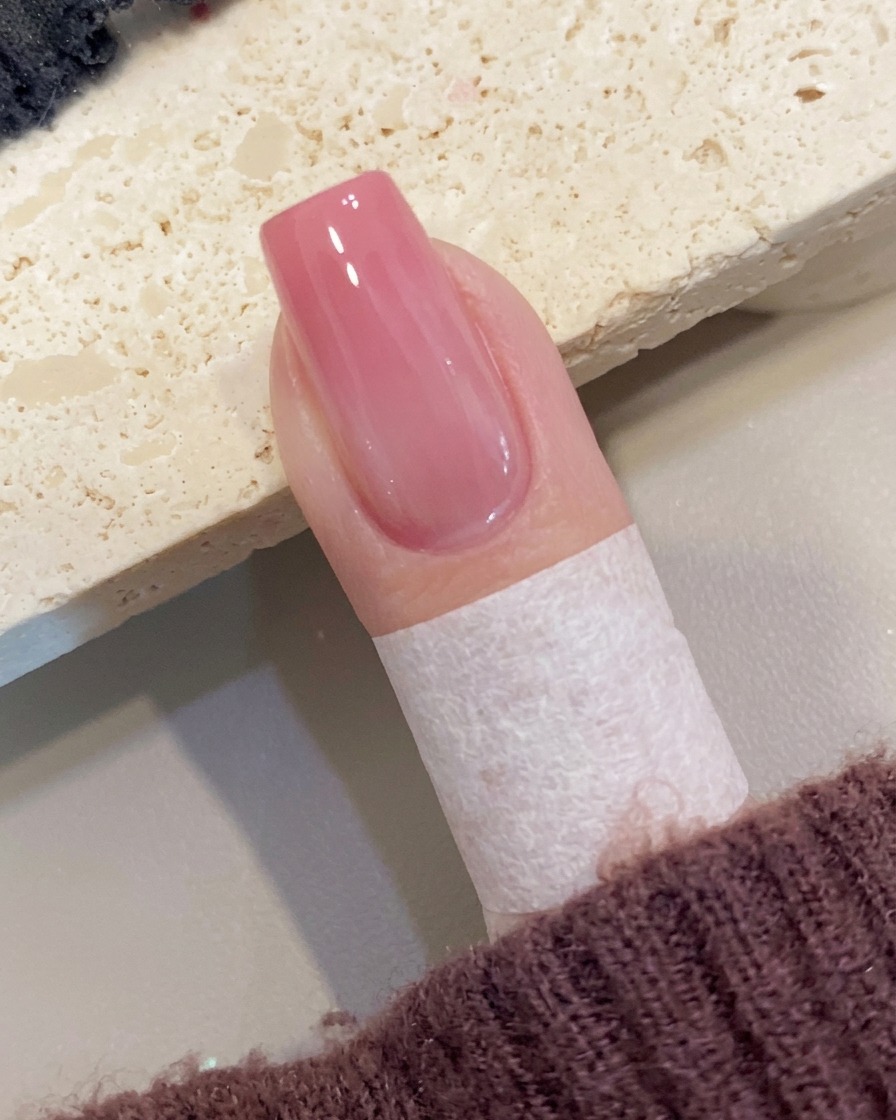 Ein Pinsel trägt eine letzte Schicht klaren Hochglanz-Top-Coats auf einen Pfirsich-Ombré-Nagel auf.
