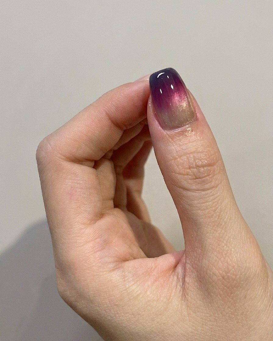 Ein Pinsel trägt einen letzten glänzenden Top-Coat über ein fertiges blau-lila Ombré-Design auf.