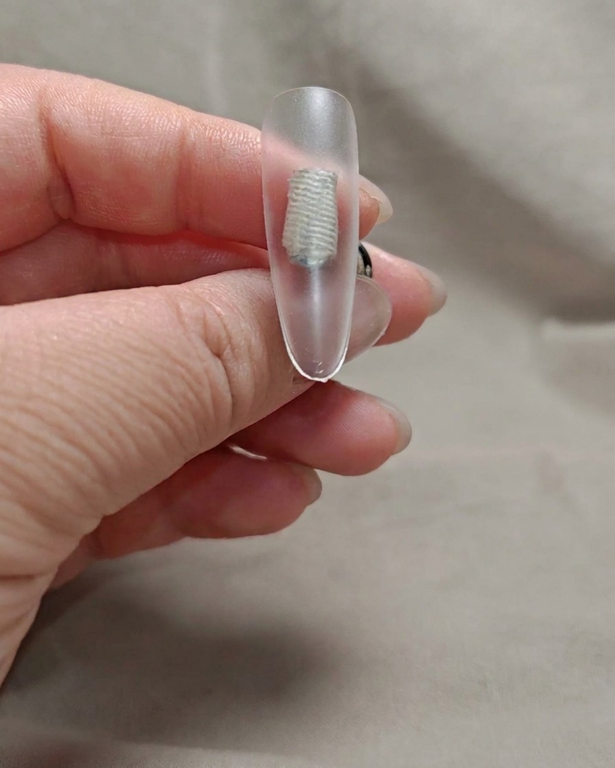 Ein Pinsel trägt eine dünne Schicht transparentes Nude-Rosa-Gel auf eine Nagelspitze auf.