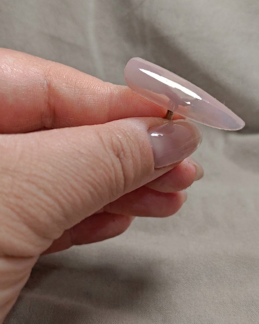 Ein Pinsel trägt eine zweite Schicht transparentes Nude-Rosa-Gel auf die Nagelspitze auf.