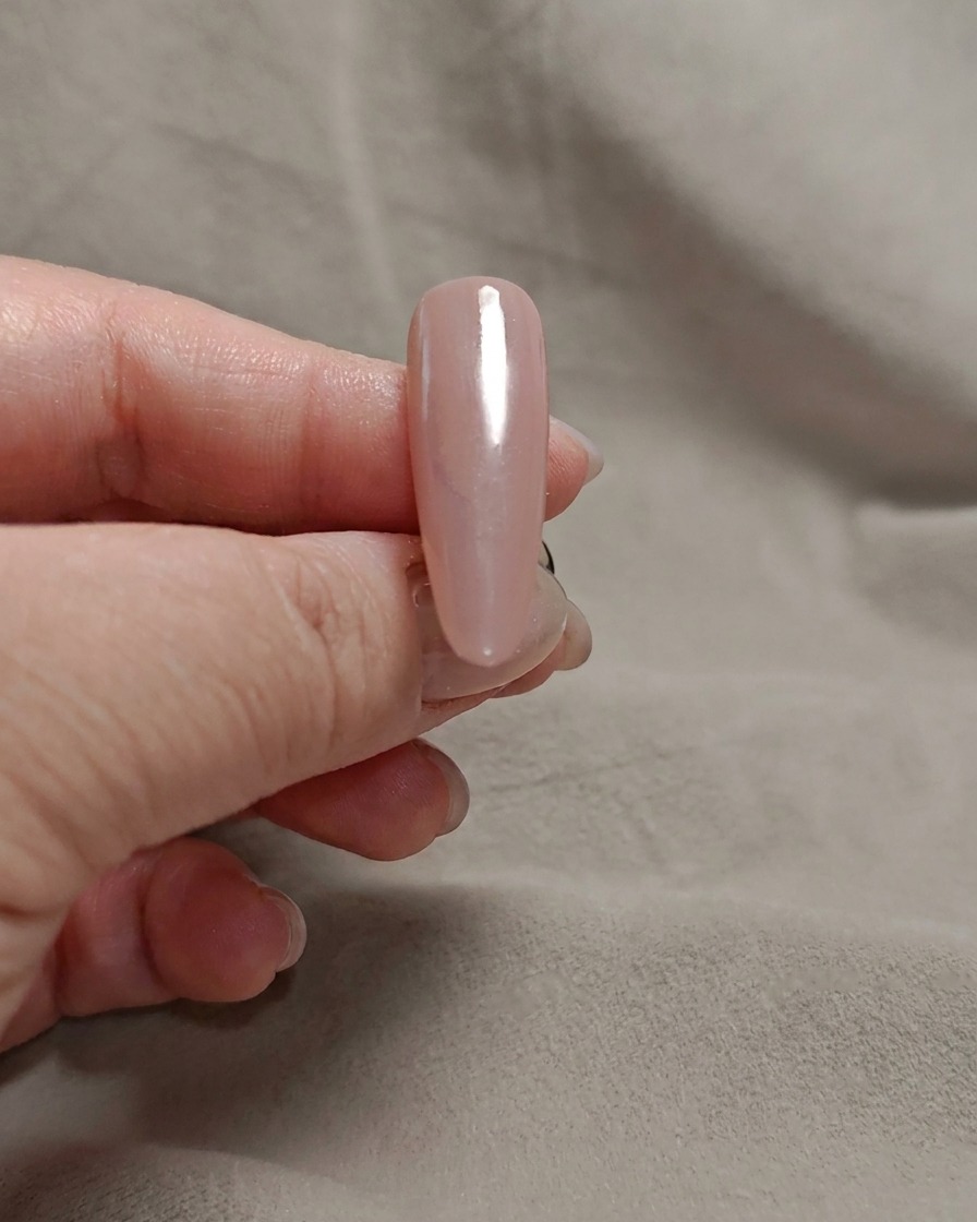 Ein Make-up-Schwamm tupft milchig weißes Gel auf die Spitze eines rosa Nagels.
