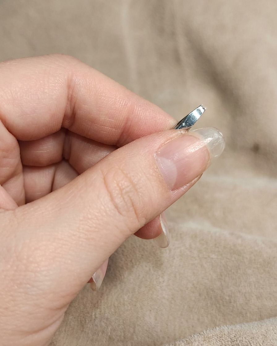 Eine Nahaufnahme zeigt einen manikürten Nagel, der mit einem Finger mit weißem Chrome-Puder eingerieben wird.