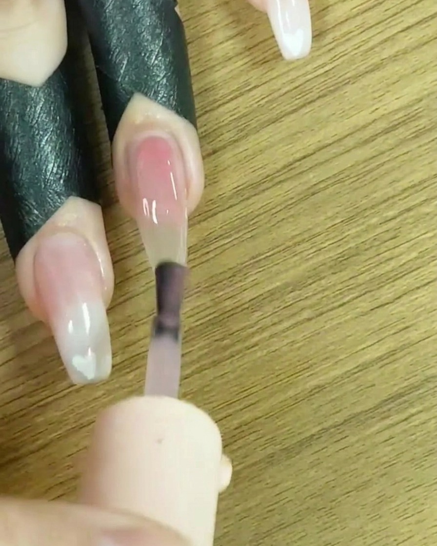 Ein Pinsel trägt helles Nude-Gel auf die gesamte Nageloberfläche auf.