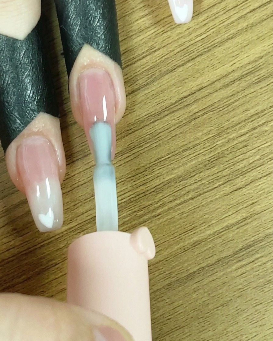 Ein Pinsel trägt eine Linie weißes Gel auf die Nagelspitze auf.