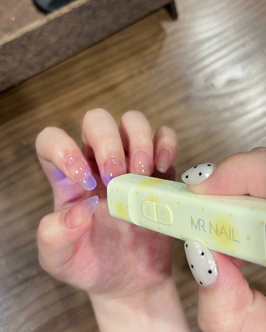 Nägel, die unter einer kleinen, tragbaren MR NAIL UV-Lampe zum Aushärten positioniert sind.