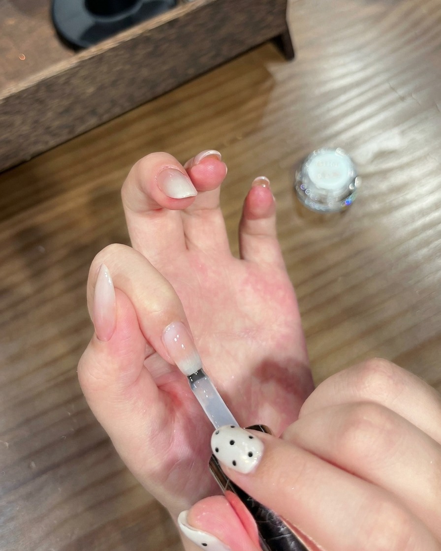 Ein Pinsel trägt einen klaren Top Coat auf einen fertigen Ombré-Nagel mit Chrome-Effekt auf.