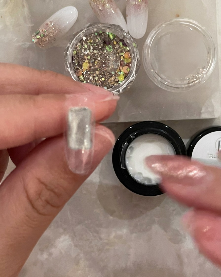 Ein feiner Pinsel trägt eine dünne, klare Schicht Base Coat auf die Mitte eines transparenten Kunstnageltips auf.