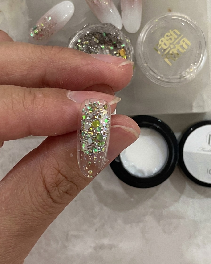 Nahaufnahme eines Nageltips in einer UV-Lampe, wobei die Glitzerschicht ausgehärtet aussieht.