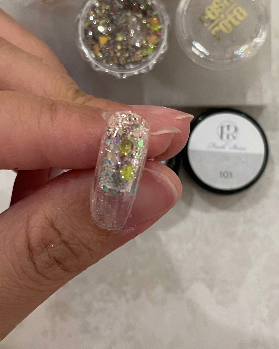 Nahaufnahme eines Nageltips unter Licht, der zeigt, wie das Struktur-Gel über dem Glitzer ausgehärtet wird.