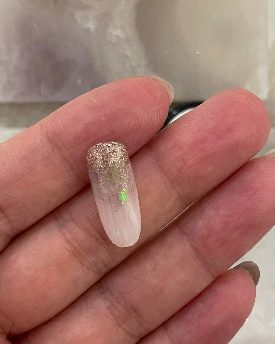 Ein Fingernagel mit milchig-weißem Ombré-Verlauf liegt in einer UV-Nagellampe während des Aushärtungsvorgangs.