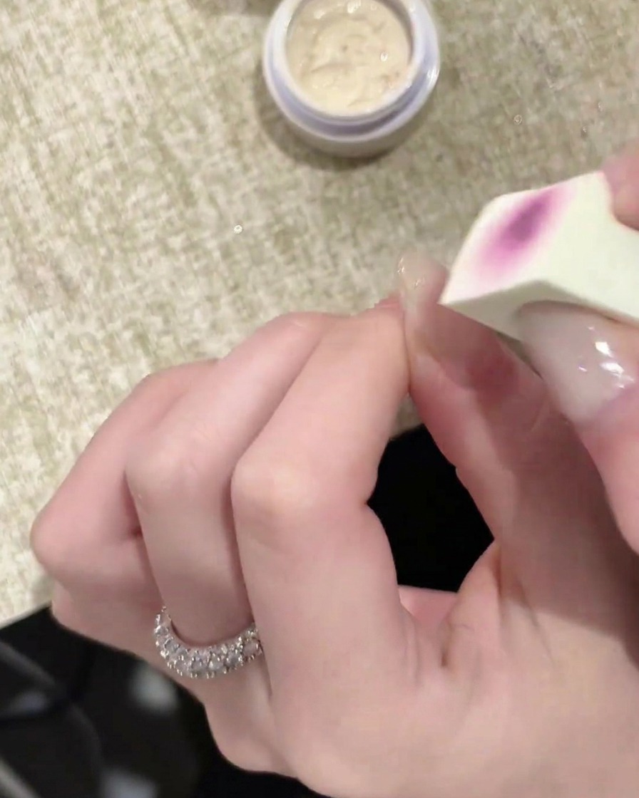 Nahaufnahme eines Schwämmchen-Applikators, der eine Schicht weißes Gel auf einen Fingernagel aufträgt.
