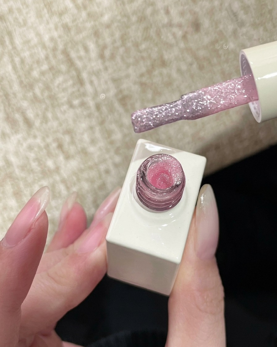 Ein Nagellackpinsel mit einem transparenten, funkelnden rosa Glitzergel, bereit zum Auftragen.