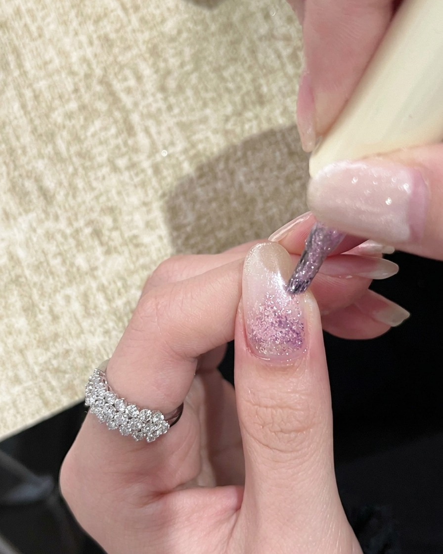 Eine Hand unter einer UV-Handlampe mit Nägeln, die einen hellrosa Ombré-Effekt zeigen.