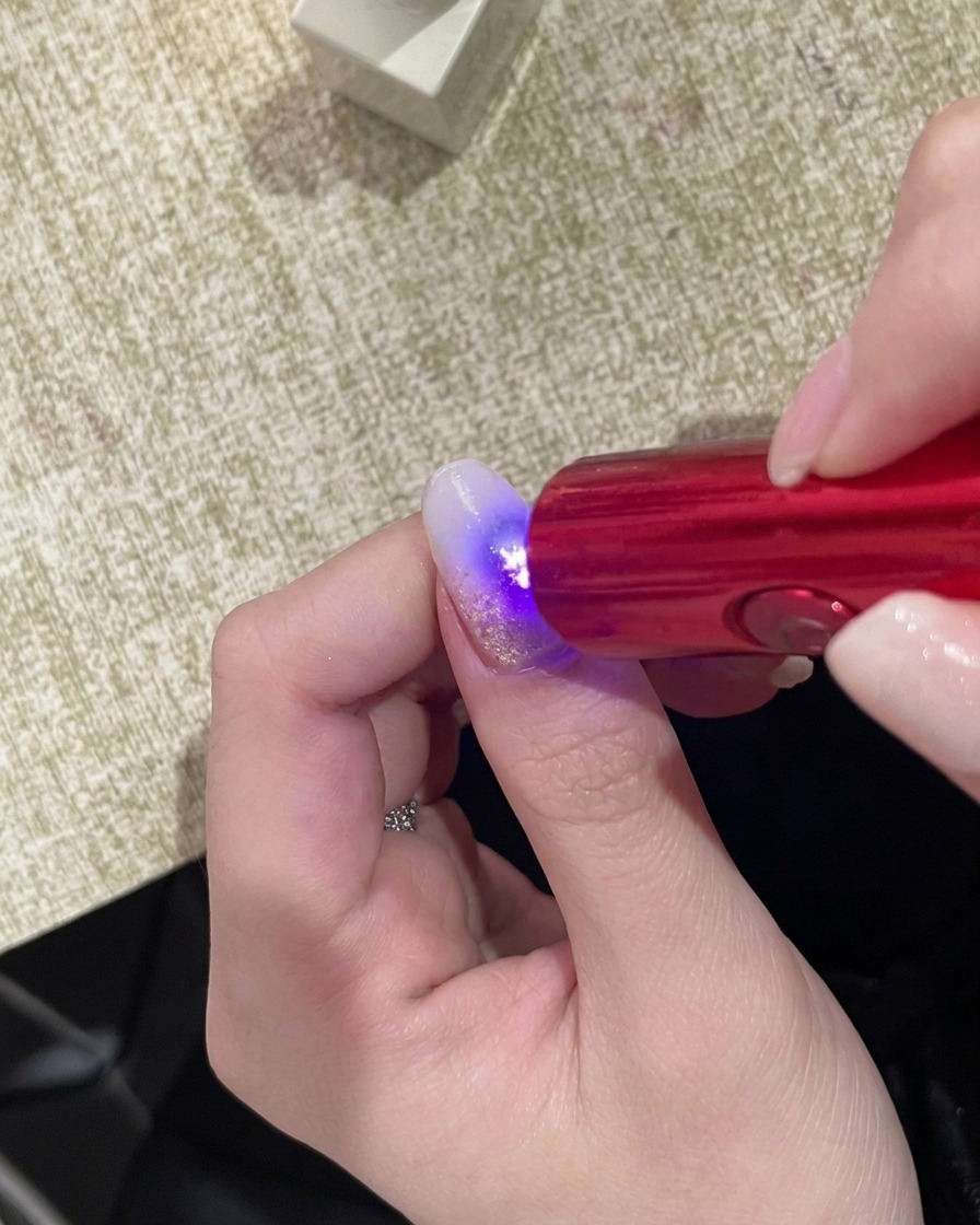 Eine Hand befindet sich unter einer kompakten UV-Handlampe, wobei die Nageloberfläche im Licht leuchtet.