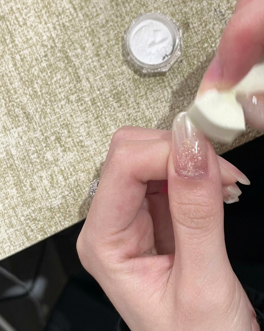 Ein Schwamm-Applikator tupft Gold Chrome Puder auf den freien Rand eines Nagels.