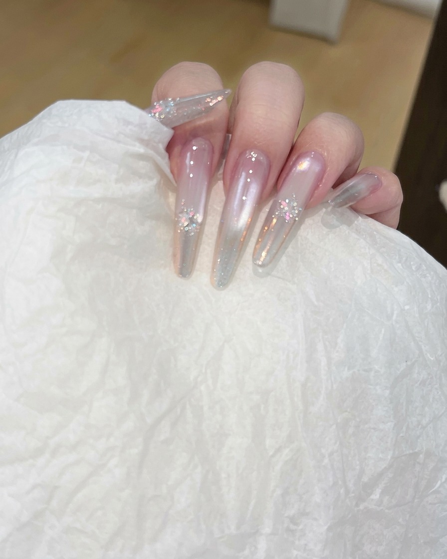 Nahaufnahme einer Hand, die mit einem Pad die Oberfläche eines langen, klaren Nagels reinigt.