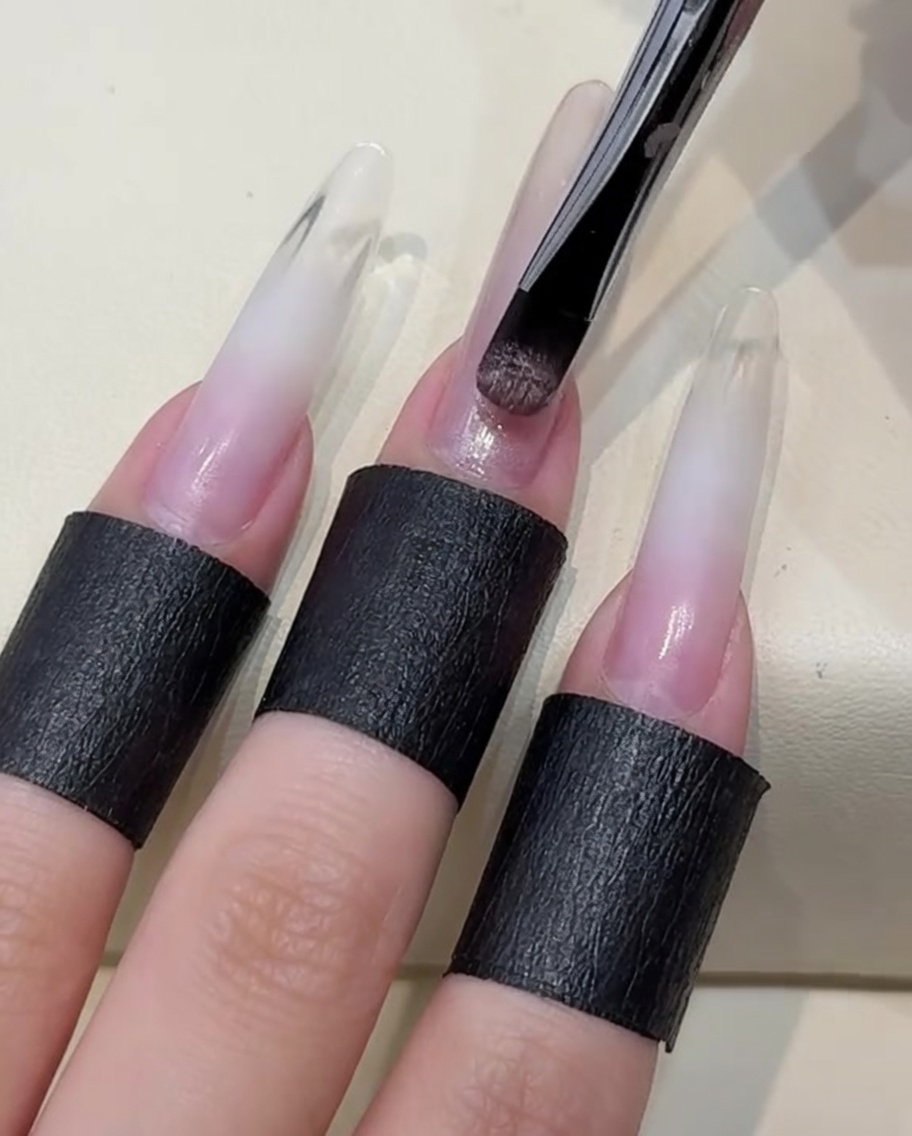Ein Pinsel trägt eine Schicht helles, nudefarbenes Cat-Eye-Gel auf den Nagel auf.