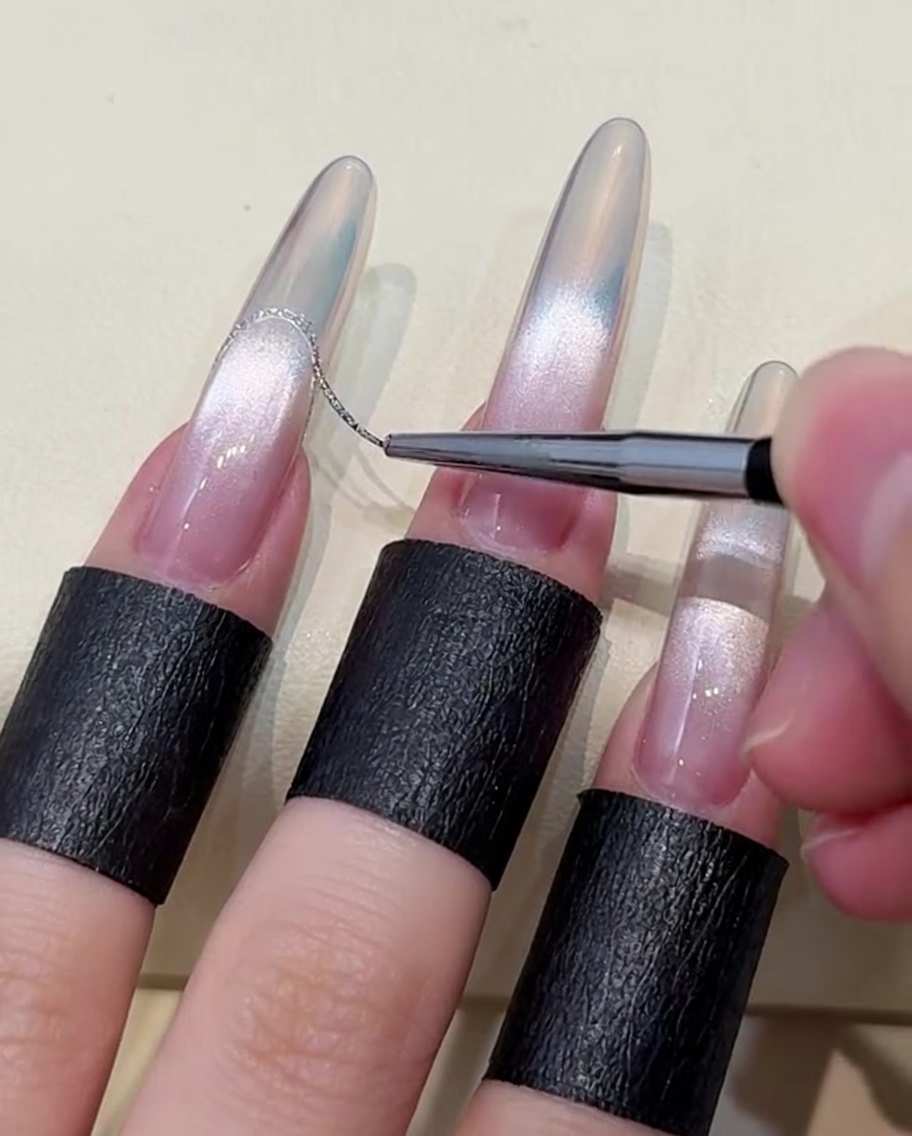 Nahaufnahme eines feinen Liner-Pinsels, der eine dünne Linie aus Platin-Silber-Gel zieht, um eine French-Spitze auf einem Aurora-Verlauf zu erzeugen.