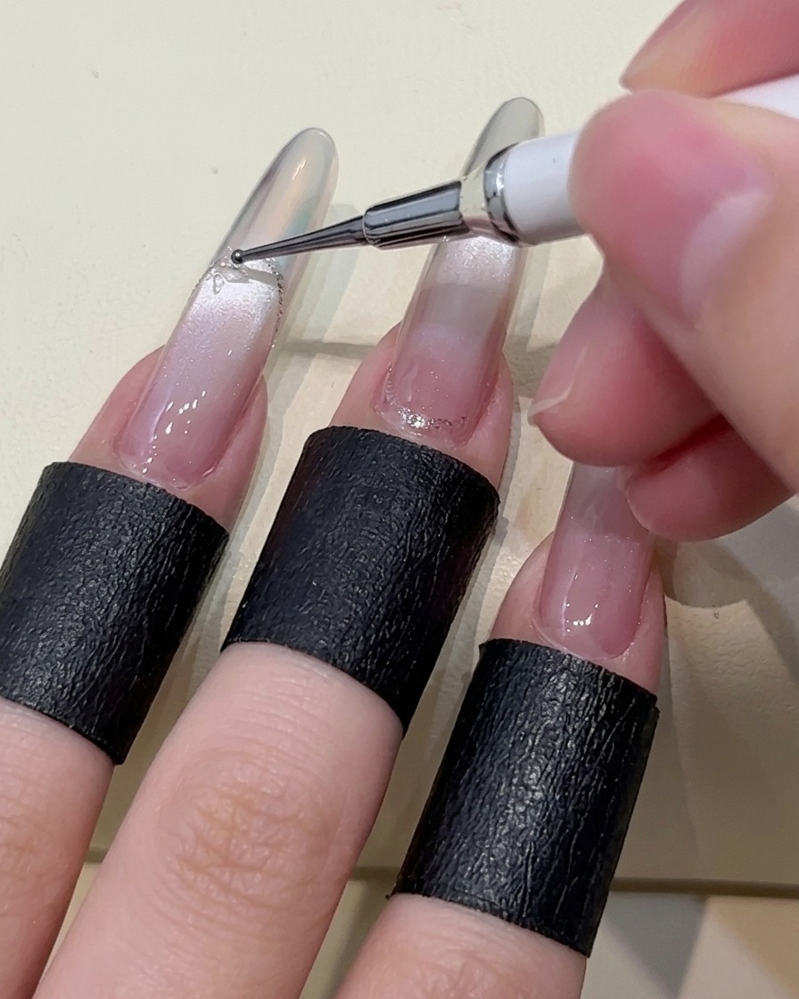 Nahaufnahme eines Dotting-Tools, das kleine Punkte aus klarem Klebegel auf die Oberfläche eines manikürten Nagels setzt.