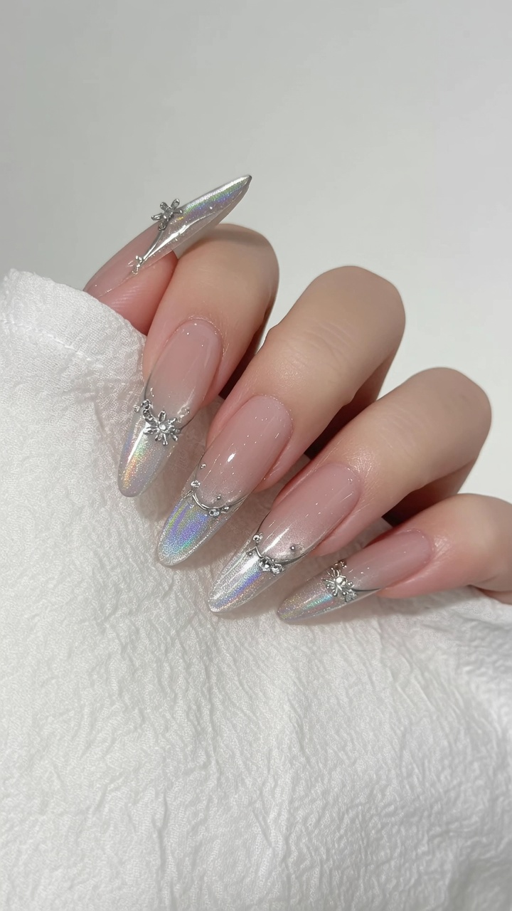 Lange, mandelförmige Nägel mit einer sanften Nude-Cat-Eye-Basis, Aurora-Chrome-Gradient-Spitzen und zarten Kristallverzierungen.
