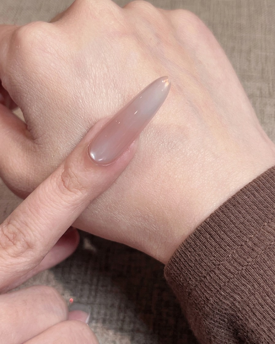 Nahaufnahme einer Nagelpinsel-Applikation einer dünnen, glatten Schicht Nude-Gel-Lack auf einem vorbereiteten Nagel.