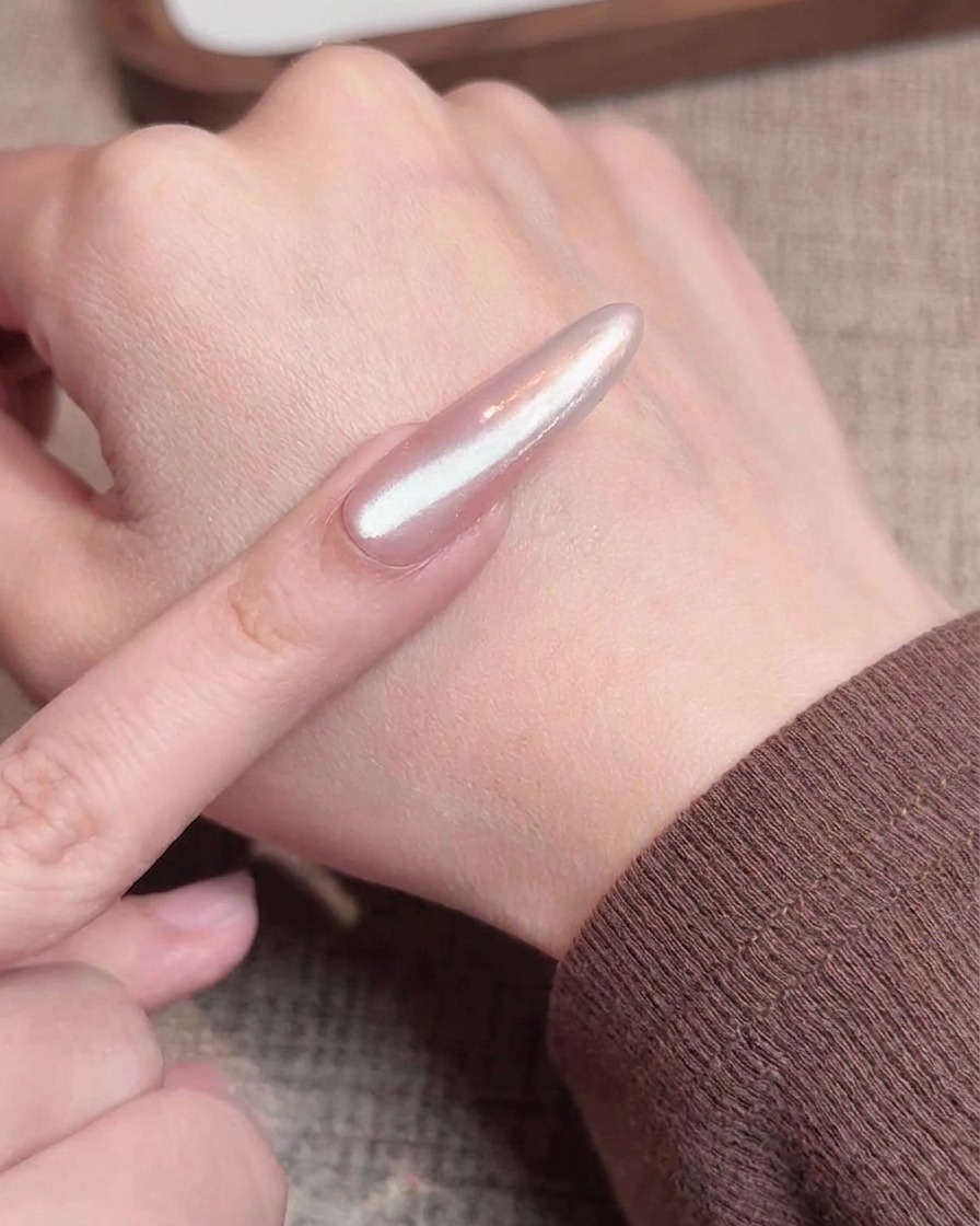 Ein Pinsel trägt eine Schicht schimmerndes Cat-Eye-Gel über einen Nagel mit Chrom-Verlauf auf.