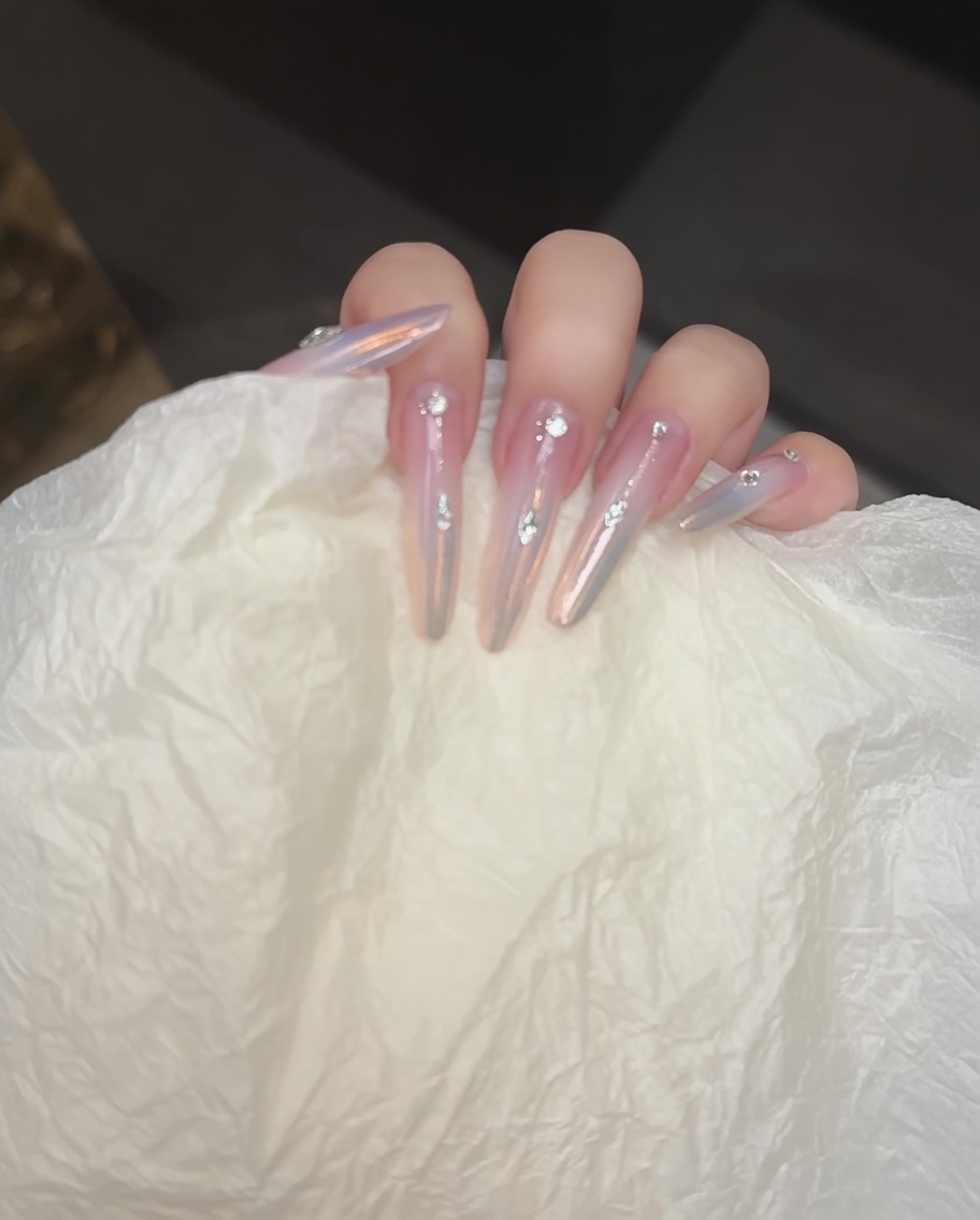 Eine Nagelbürste trägt eine nudefarbene Basisschicht auf den Nagel auf.
