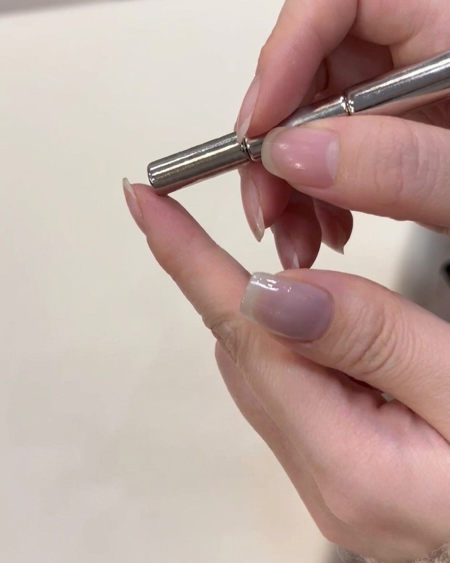 Ein Magnetwerkzeug wird knapp über den frisch beschichteten Cat-Eye-Nagel gehalten, um die Partikel zu formen.