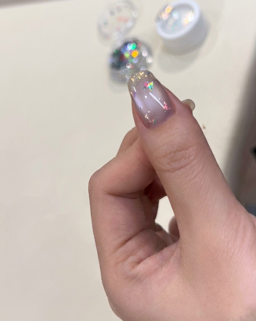 Ein Pinsel trägt glänzenden Top Coat über den mit Flakies und Schmetterling verzierten Nagel auf.