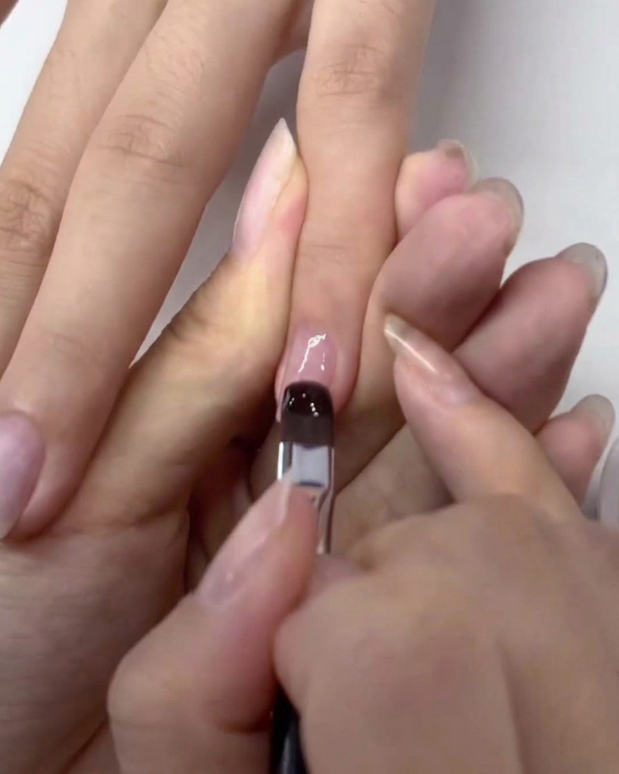 Ein Pinsel trägt eine klare Schicht Gel-Base-Coat auf einen vorbereiteten Naturnagel auf.