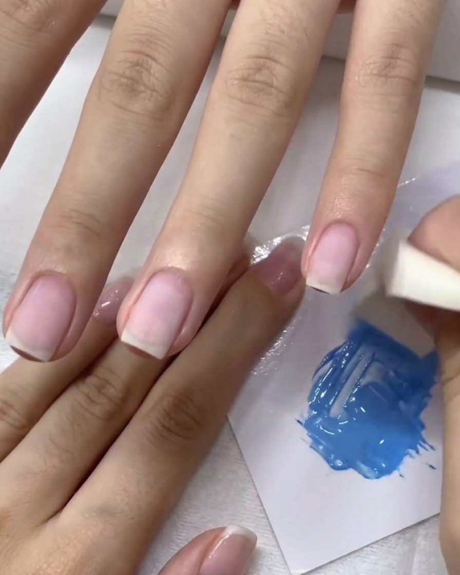 Ein Kosmetikschwamm tupft blaues Gel auf einen Fingernagel, um einen Ombré-Effekt zu erzeugen.