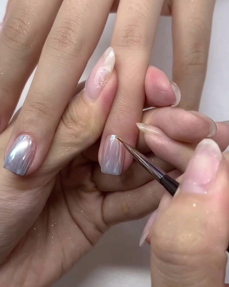 Ein kleiner Nagelpinsel trägt eine letzte Schicht Top Coat über den Chrome-Nägeln auf.